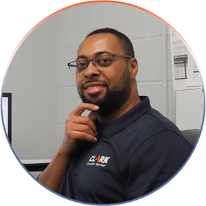 Our Team | Always Responsive, Professional, and Friendly | A man smiling with his hand to his chin, wearing a blue polo shirt and the logo for Clark Computer Services