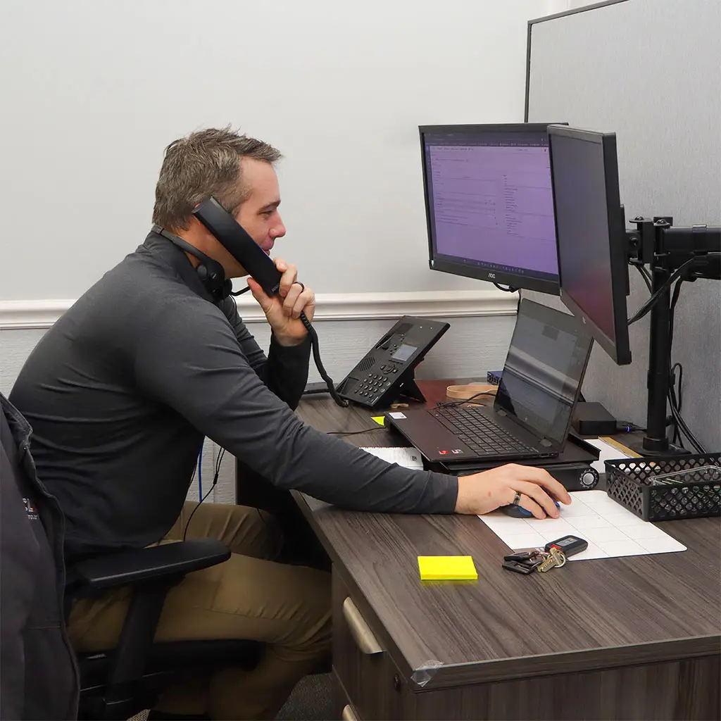 Manufacturing IT Services | Secure and Scalable IT Solutions | Clark Computer Services technician sitting at a desk, talking on the phone and looking at monitors while providing IT support for a manufacturing client